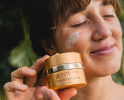 Person holding a jar of Honey Girl Organics Face & Eye Crème with a blurred natural background