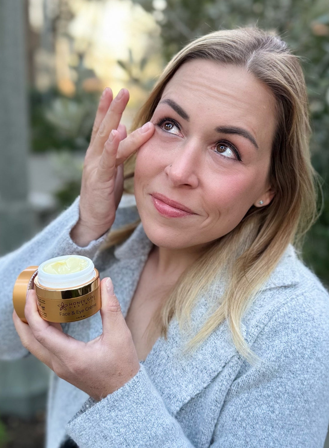 Woman applying cream to her face outdoors with a blurred natural background